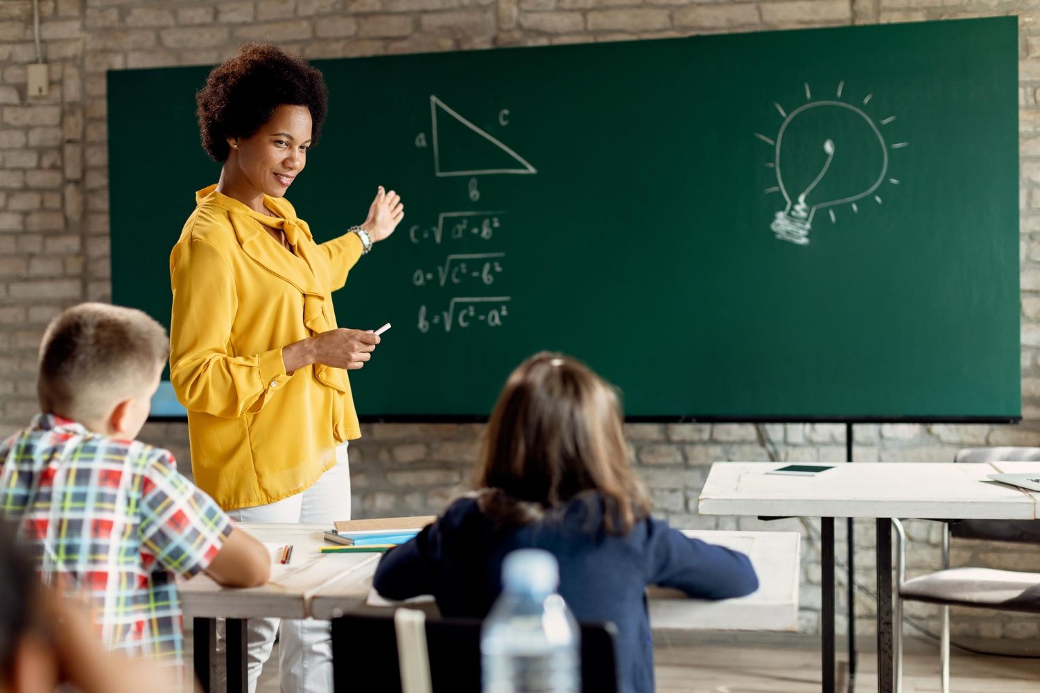 A teacher explains a maths theorem at a green chalkboard while learners watch.
