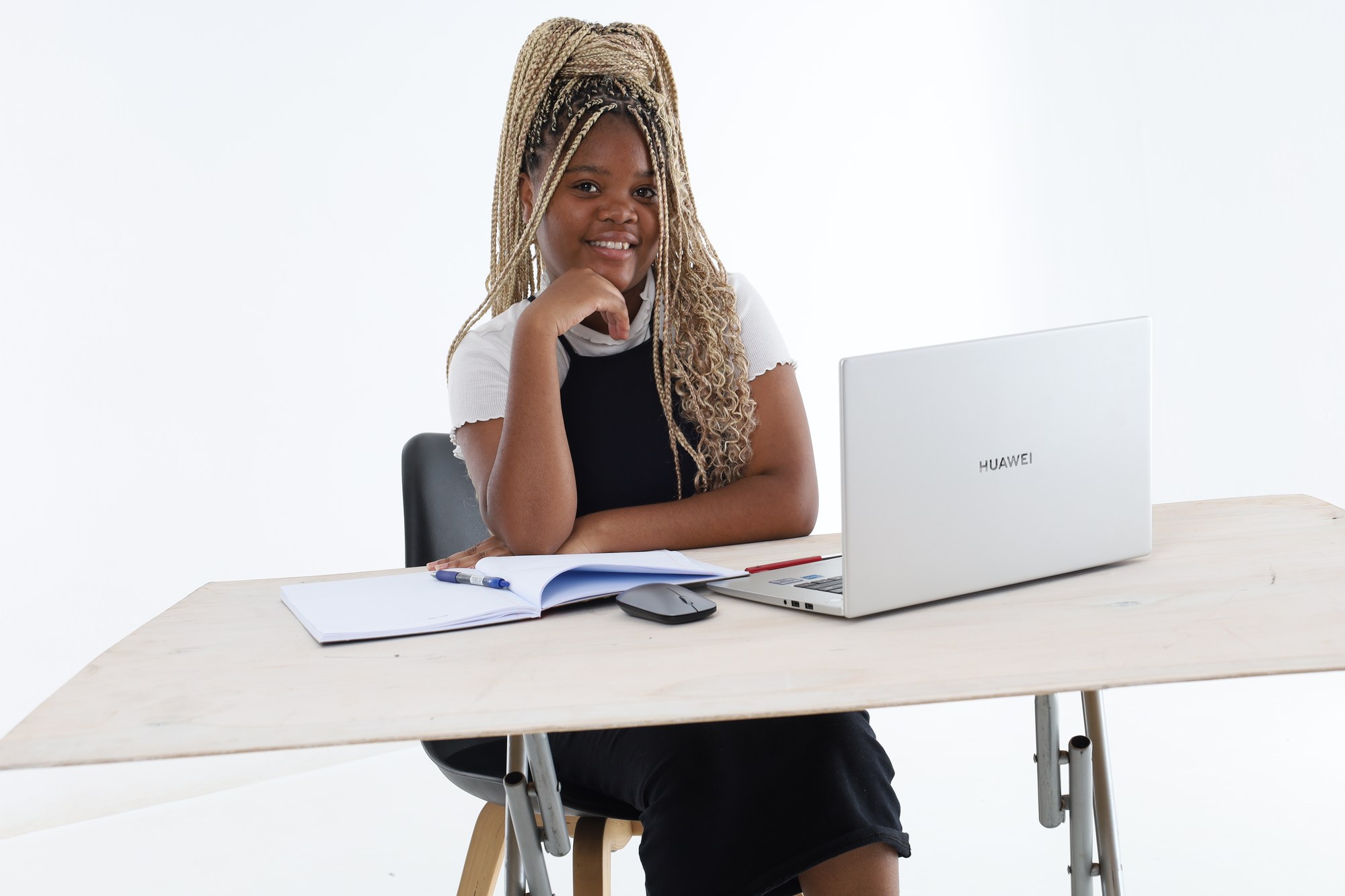 A South African high school learner sitting thoughtfully at her desk with a laptop and an open book