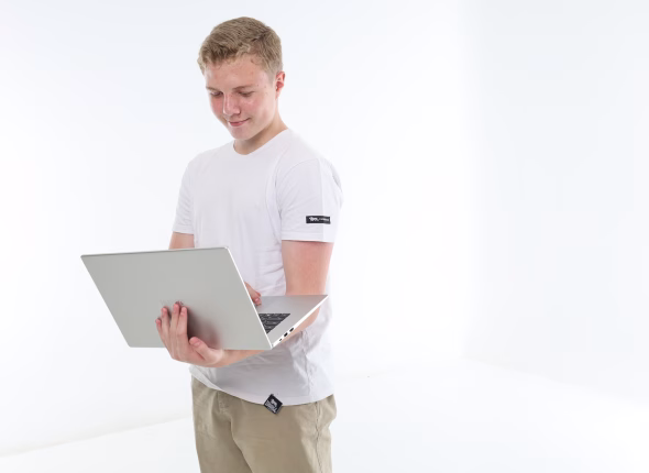 A South African high school learner standing and looking down at the laptop he is holding