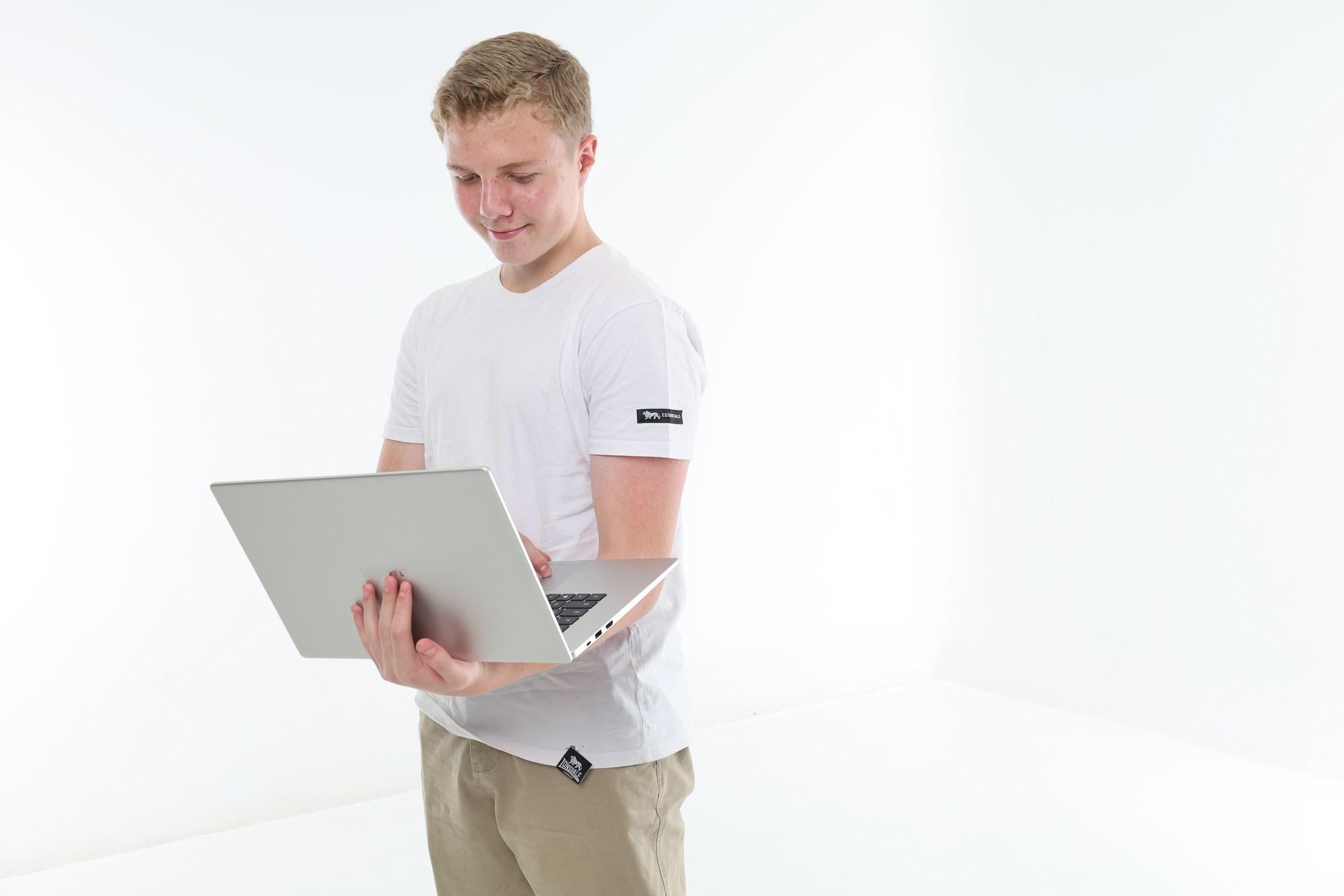 A South African high school learner standing and looking down at the laptop he is holding