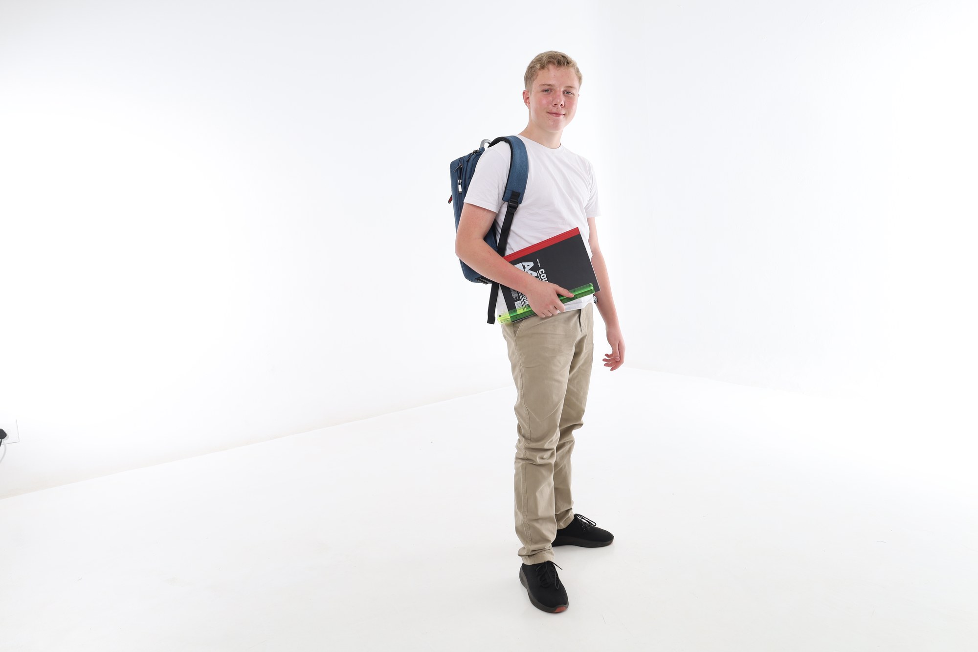 A South African high school learner standing with a backpack and carrying his books