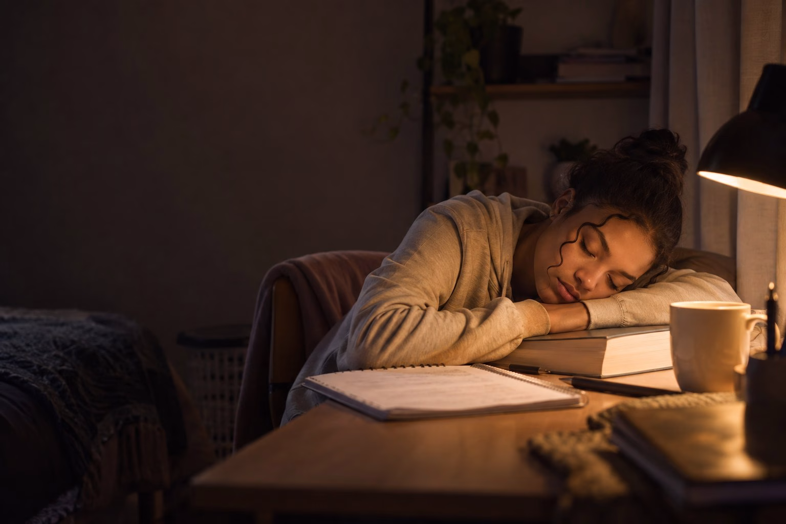 A South African Grade 12 learner asleep at her desk late at night with her head on a closed textbook and the desk lamp still on