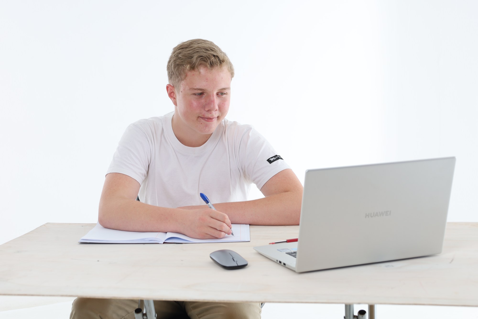A South African high school learner writing notes in his book beside an open laptop