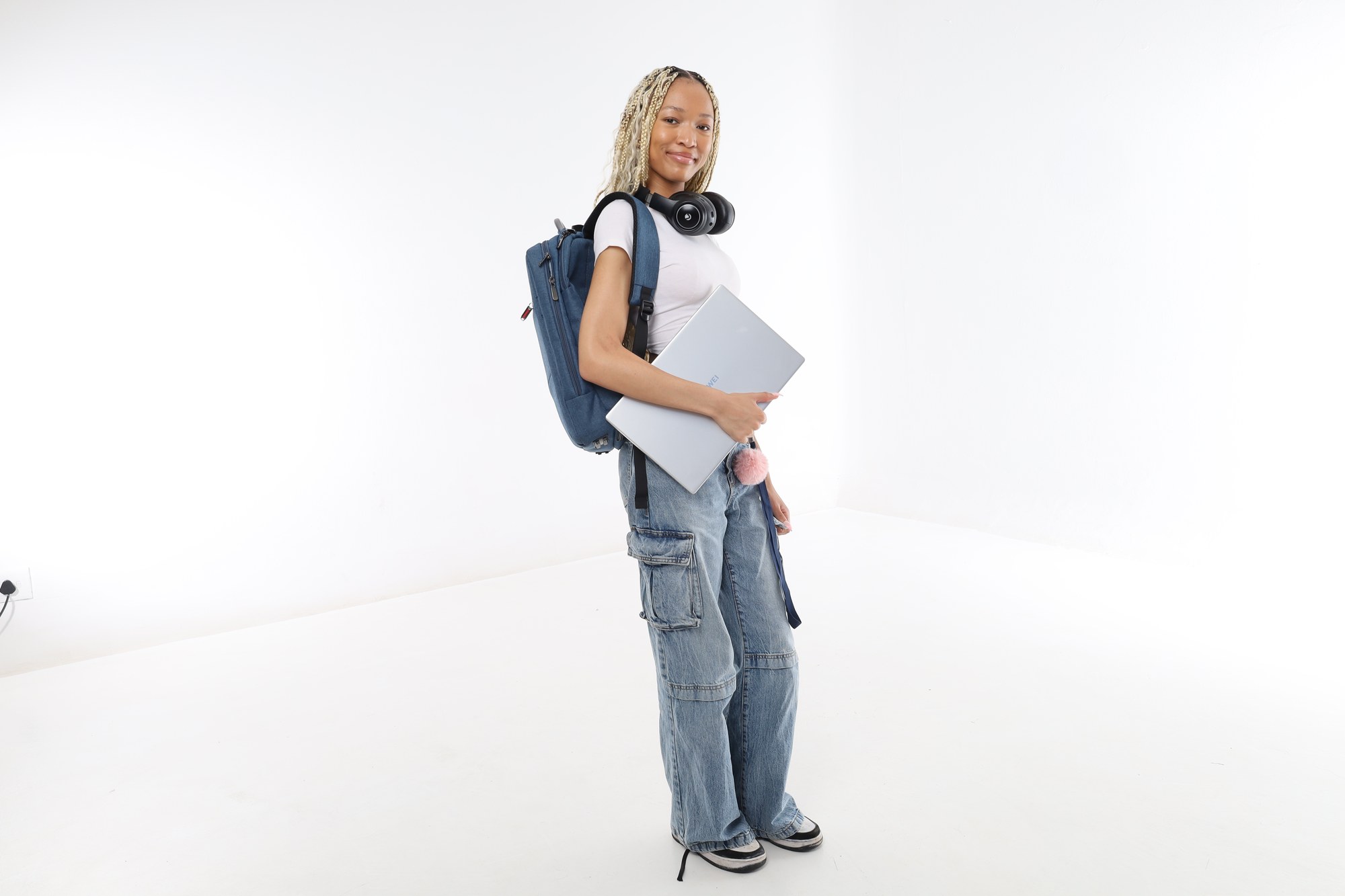 A South African student standing with a backpack, headphones and a laptop under her arm