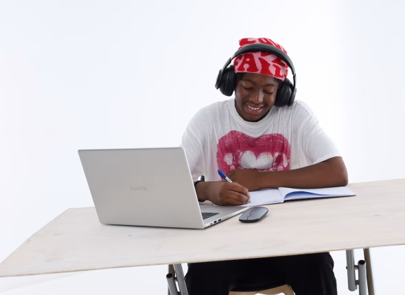 A South African teenager wearing headphones and writing in her workbook during an online lesson